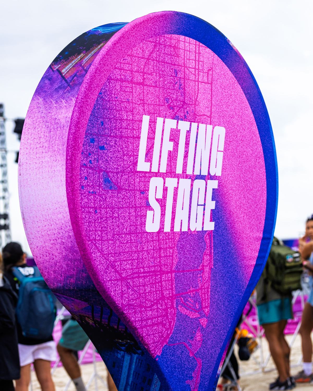 A tall Lifting Stage wayfinding sign with fans walking past
